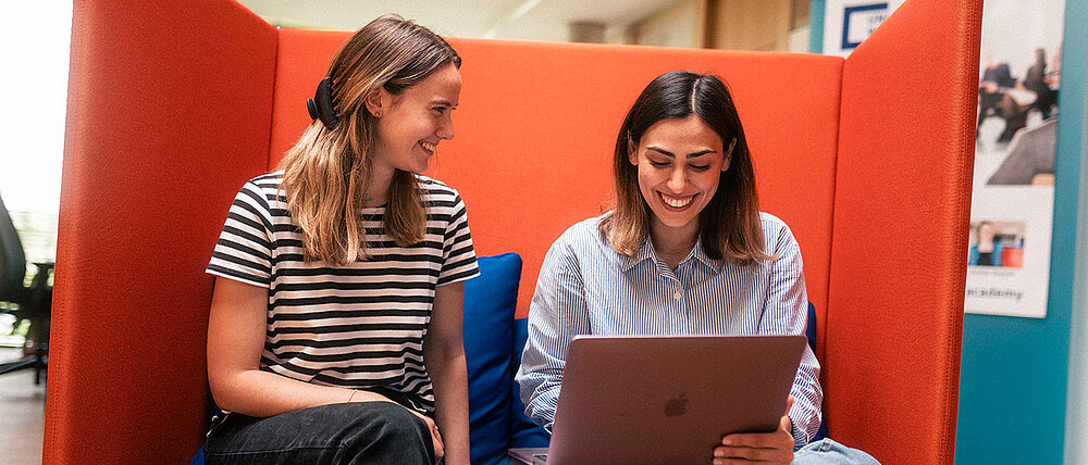 Zwei Studentinnen sitzen am Laptop und programmieren.